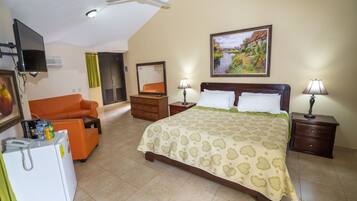 Quarto de hotel com uma cama, escrivaninha, cadeira, televisão, frigorífico e um quadro na parede.