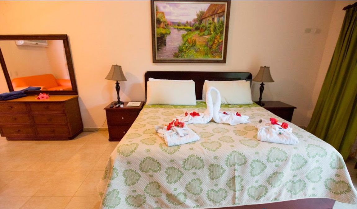 Een hotelkamer met een bed, twee nachtkastjes, een dressoir en een schilderij aan de muur.