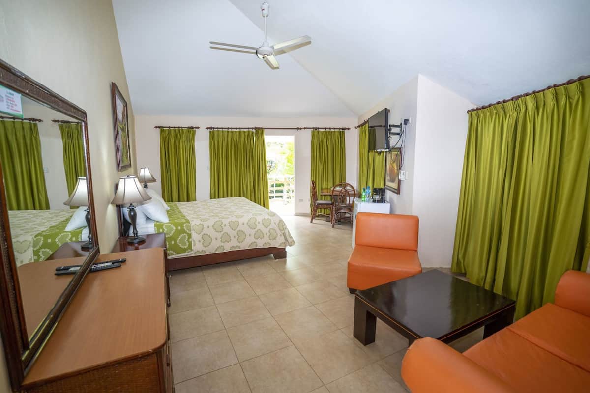 A hotel room with a bed, two chairs, a desk, a ceiling fan, and a window with curtains.