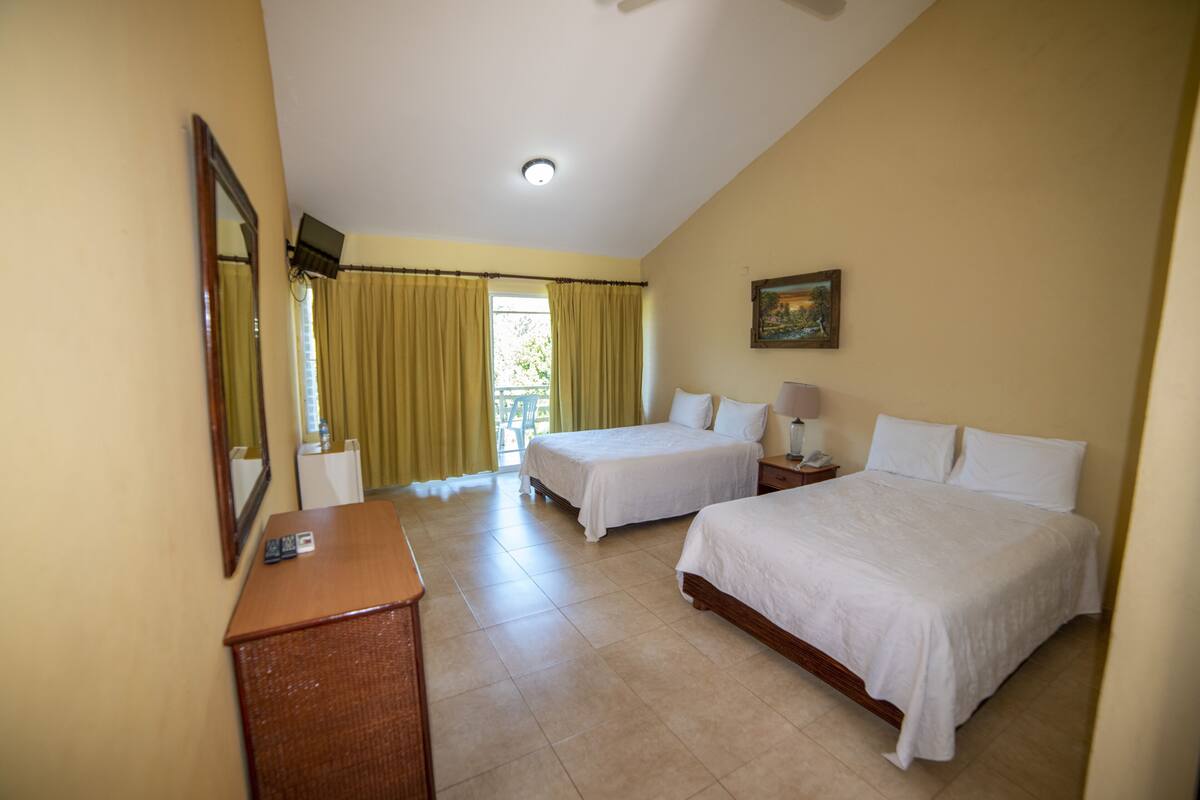 A hotel room with two beds, a desk, a chair, a TV, and a window with curtains.