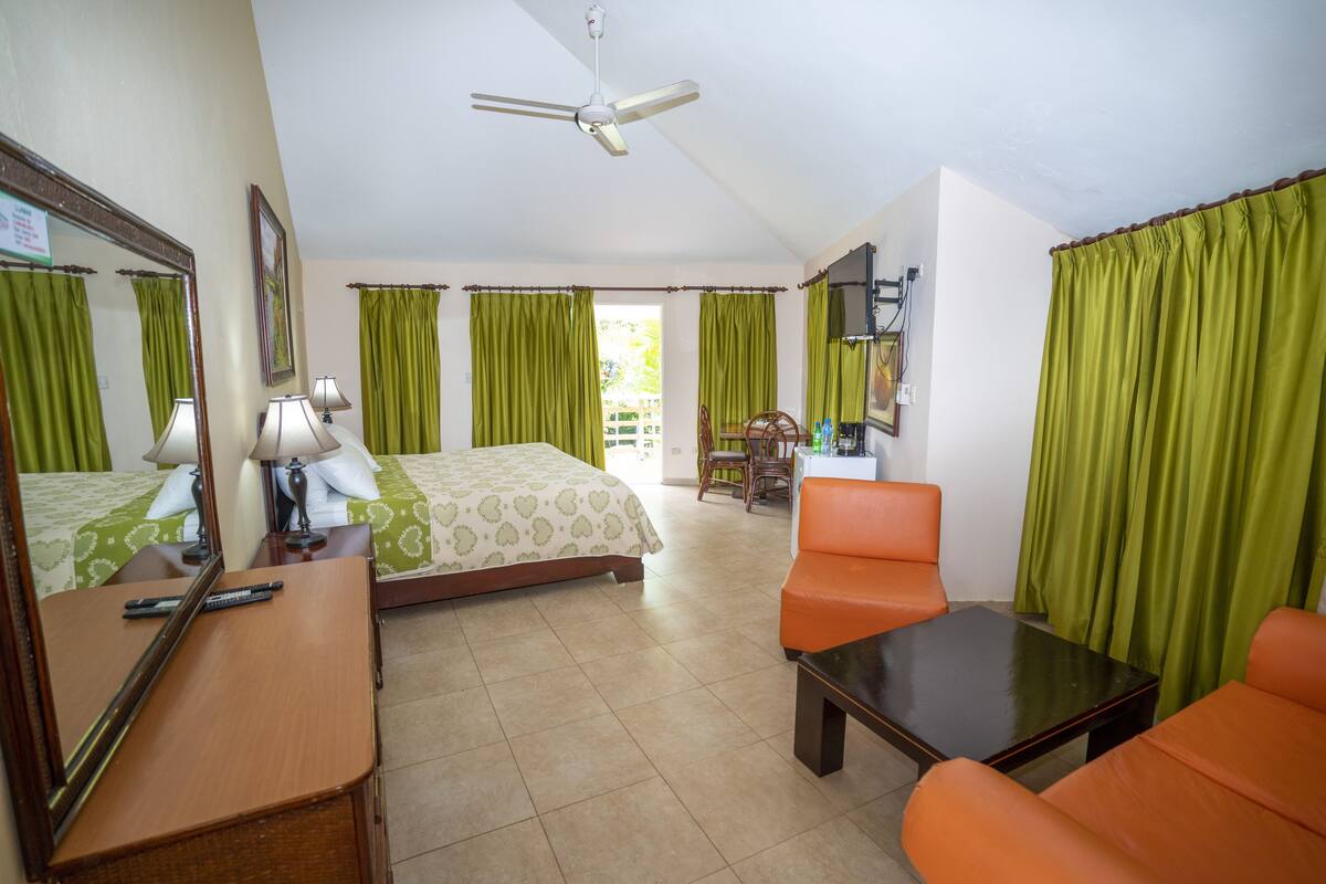 A hotel room with a bed, two chairs, a desk, a mirror, and a ceiling fan.