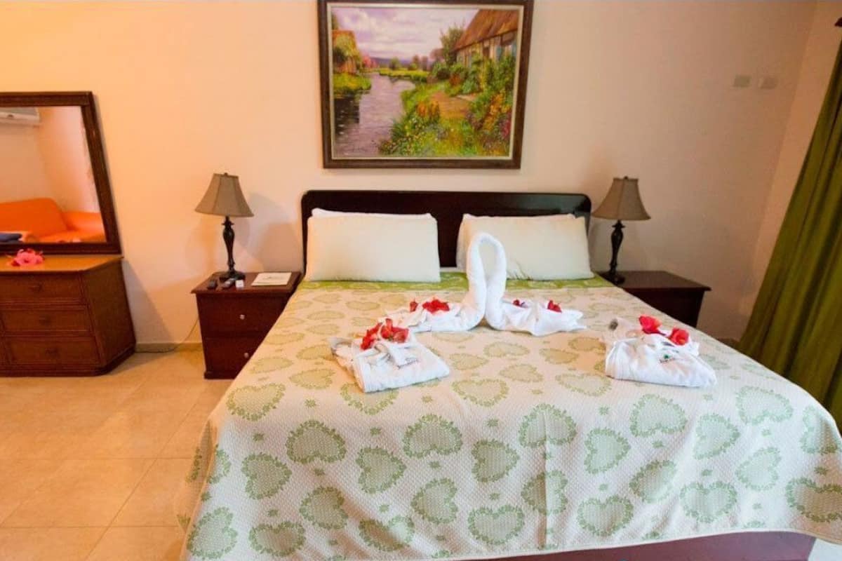 A hotel room with a bed, two nightstands, a dresser, a painting, and a green curtain.
