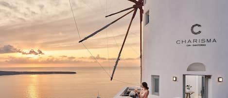 A seaside hotel with a view of the sea, a windmill, and a woman standing by a window.