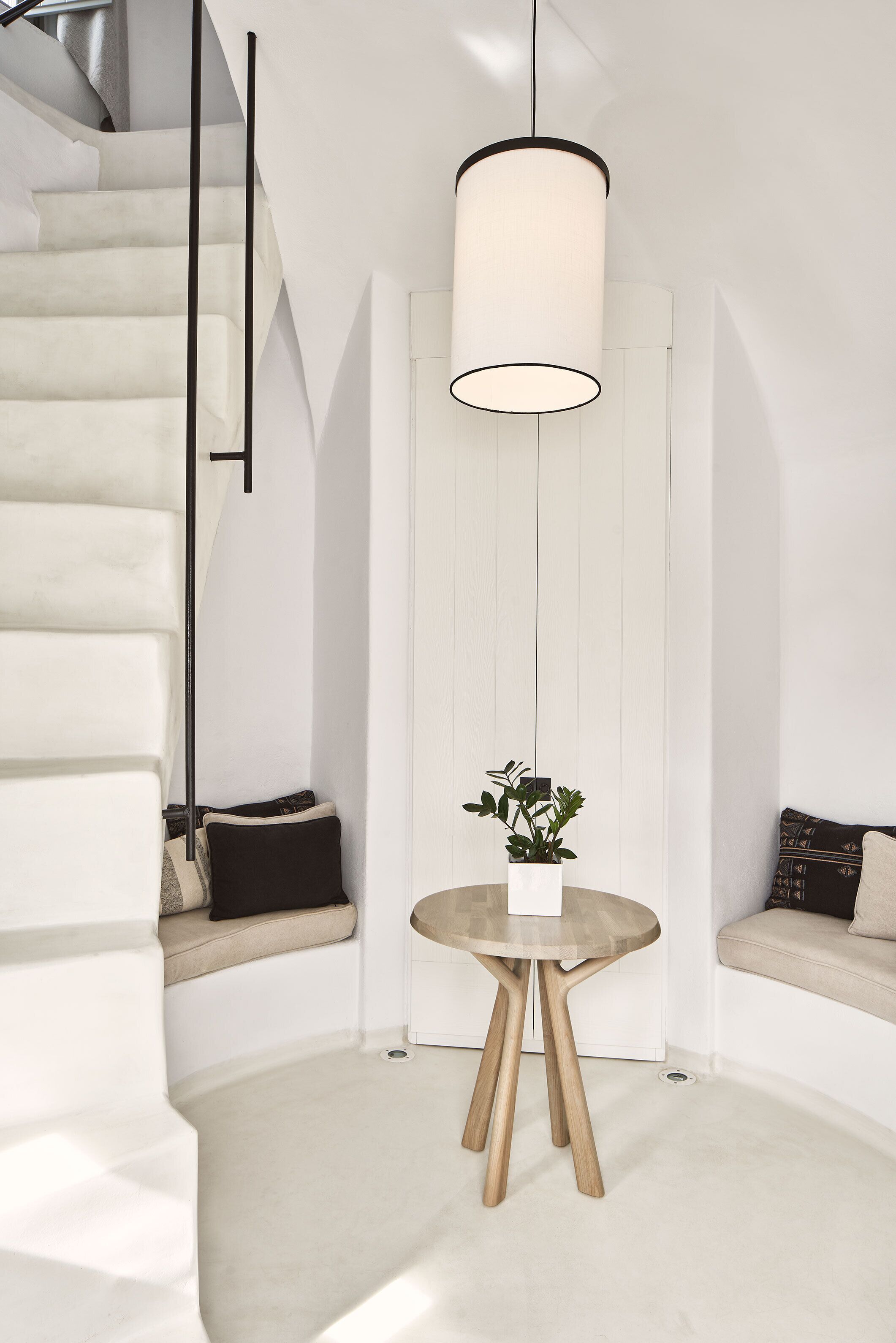 Un intérieur moderne avec un escalier, une table ronde en bois agrémentée d’une plante et un luminaire suspendu.