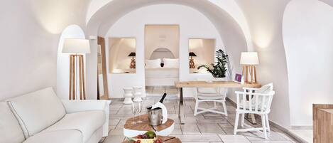 A modern living room with a white sofa, a wooden coffee table with fruit, a dining area with a table and chairs, and a large arched doorway.