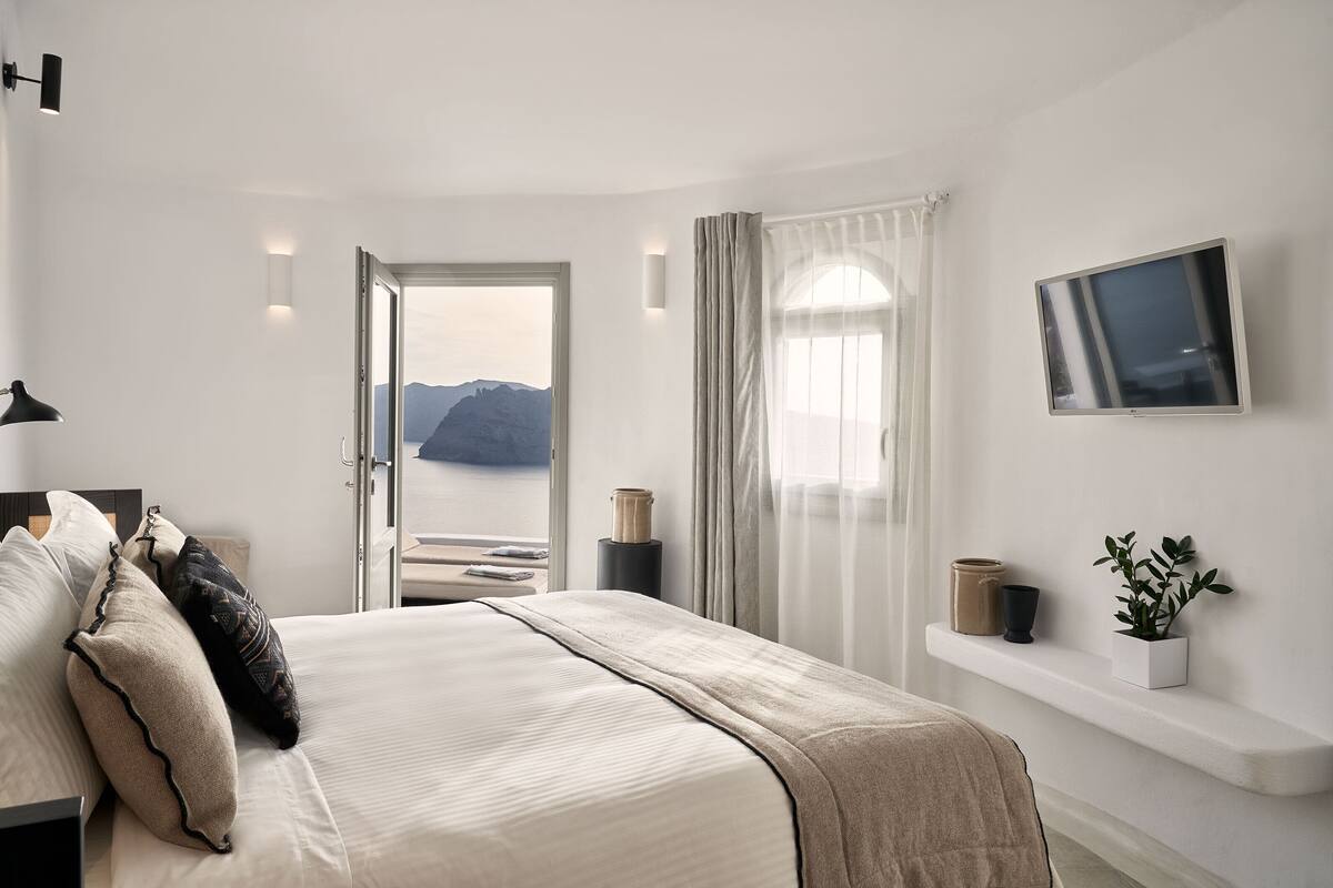 A bedroom with a bed, a TV, a window with curtains, and a view of mountains.