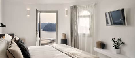 A bedroom with a bed, a TV, a window with curtains, and a view of mountains.
