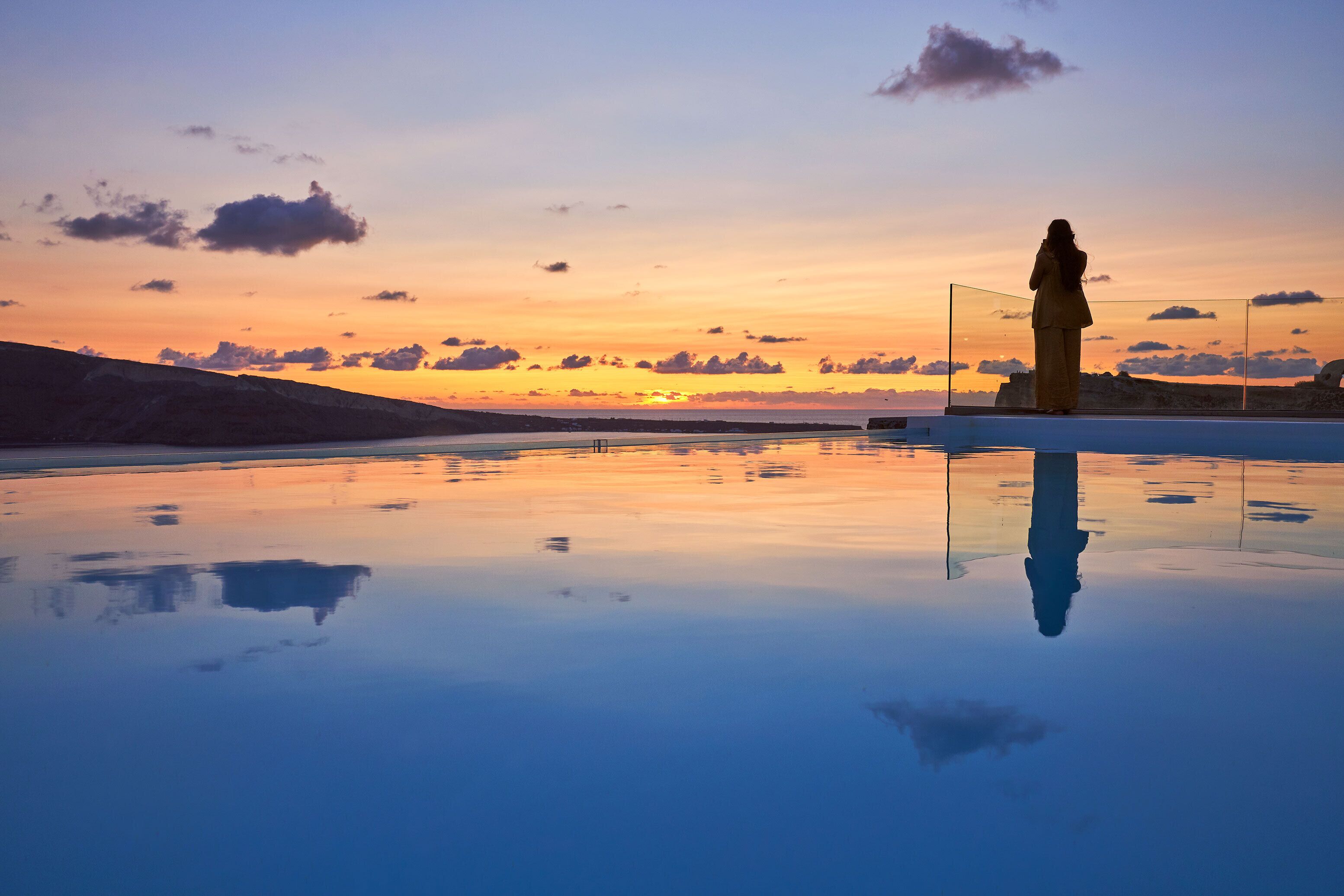 Ein friedlicher Sonnenuntergang spiegelt sich in einem See, im Vordergrund steht eine Statue.