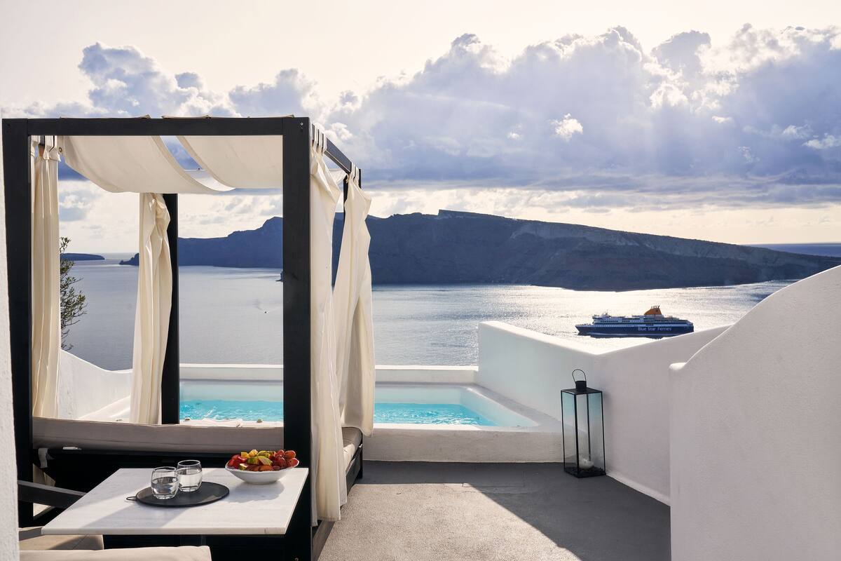 A balcony with a view of the sea, a table with a bowl of fruit, and a small pool.