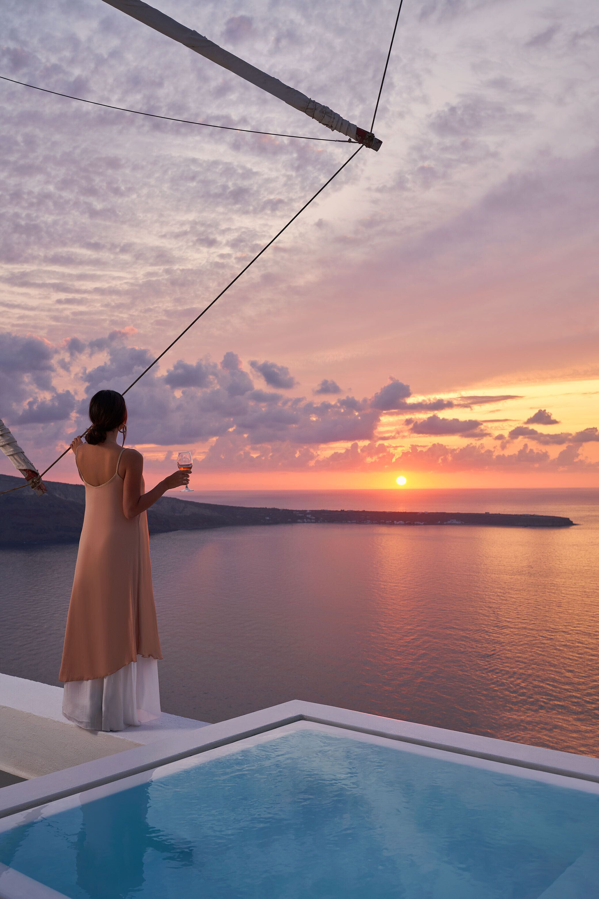 A woman overlooking a sunset from a balcony with a pool.