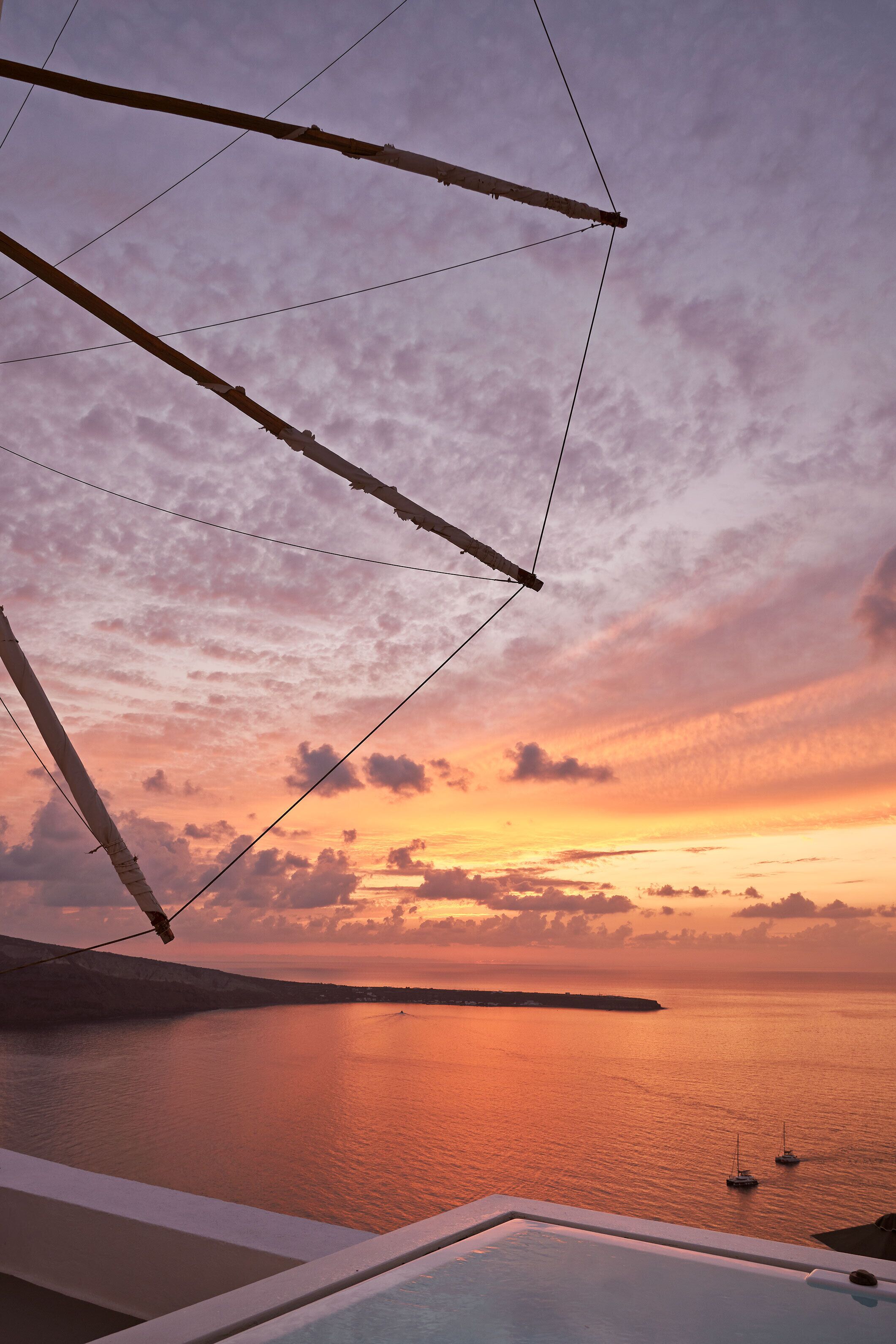 Une vue sur le coucher de soleil depuis un balcon avec piscine, donnant sur la mer et une île lointaine.