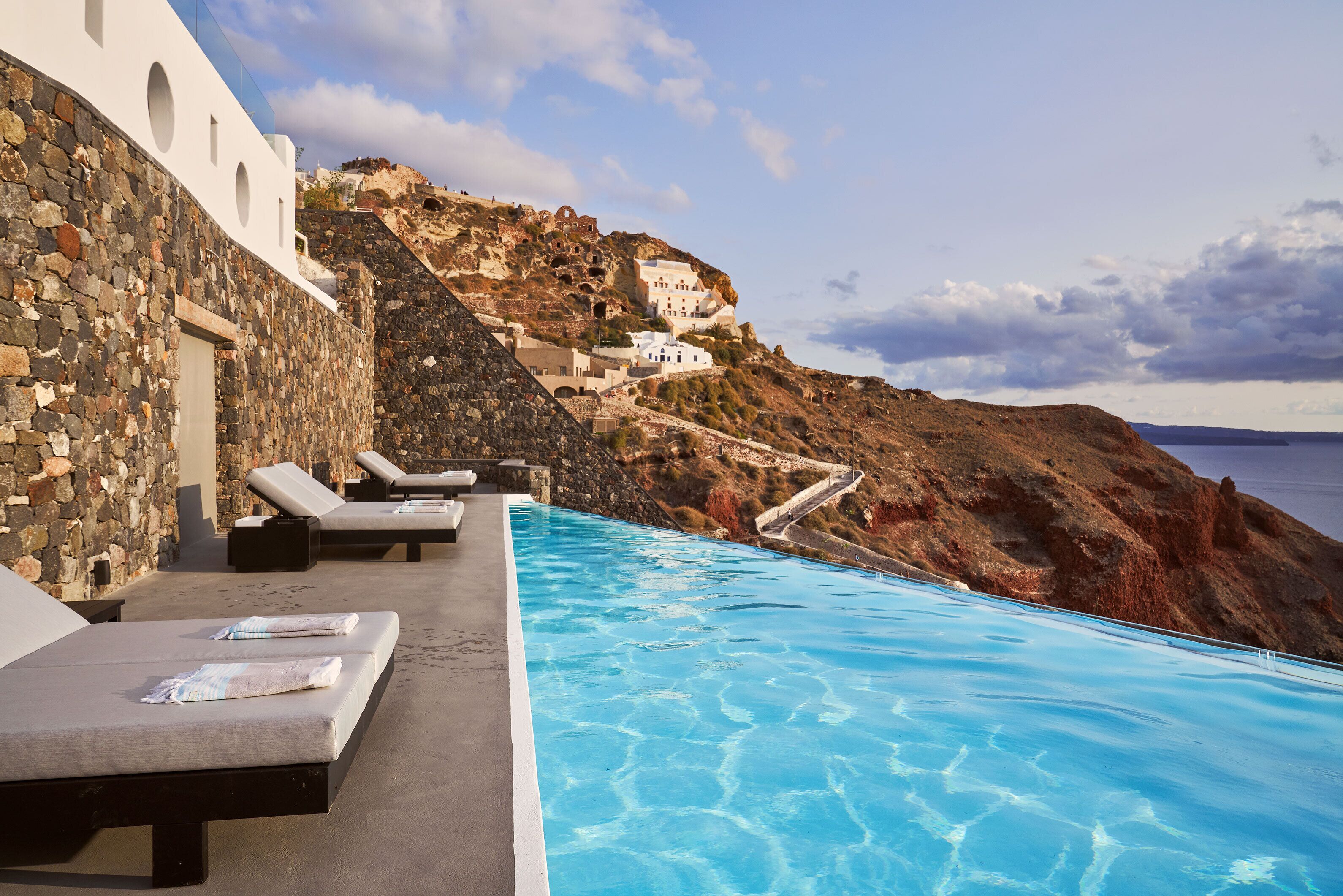Un área junto a la piscina con sillones reclinables y una pared de piedra.