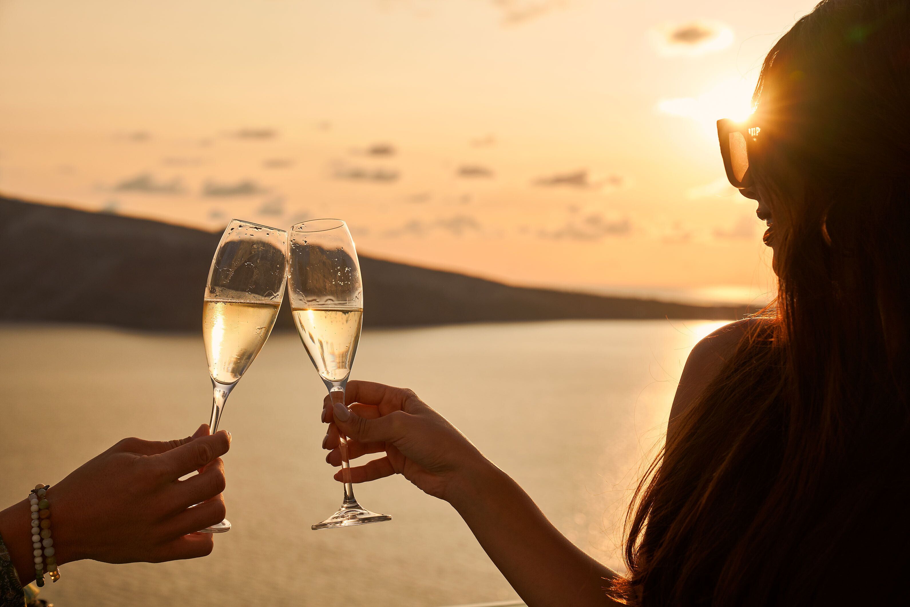 Två personer skålar med champagneglas mot en solnedgång i bakgrunden.