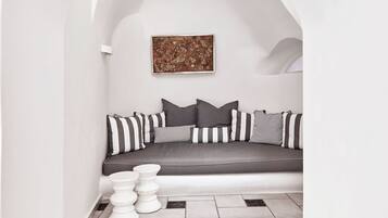 Una habitación minimalista con un arco blanco que da a una zona de estar con un sofá y cojines. Una obra enmarcada se exhibe en la pared sobre el sofá.