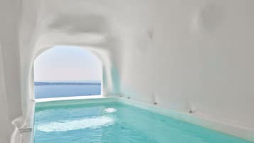 Vista despejada de una piscina con vista al mar a través de un ventanal arqueado.
