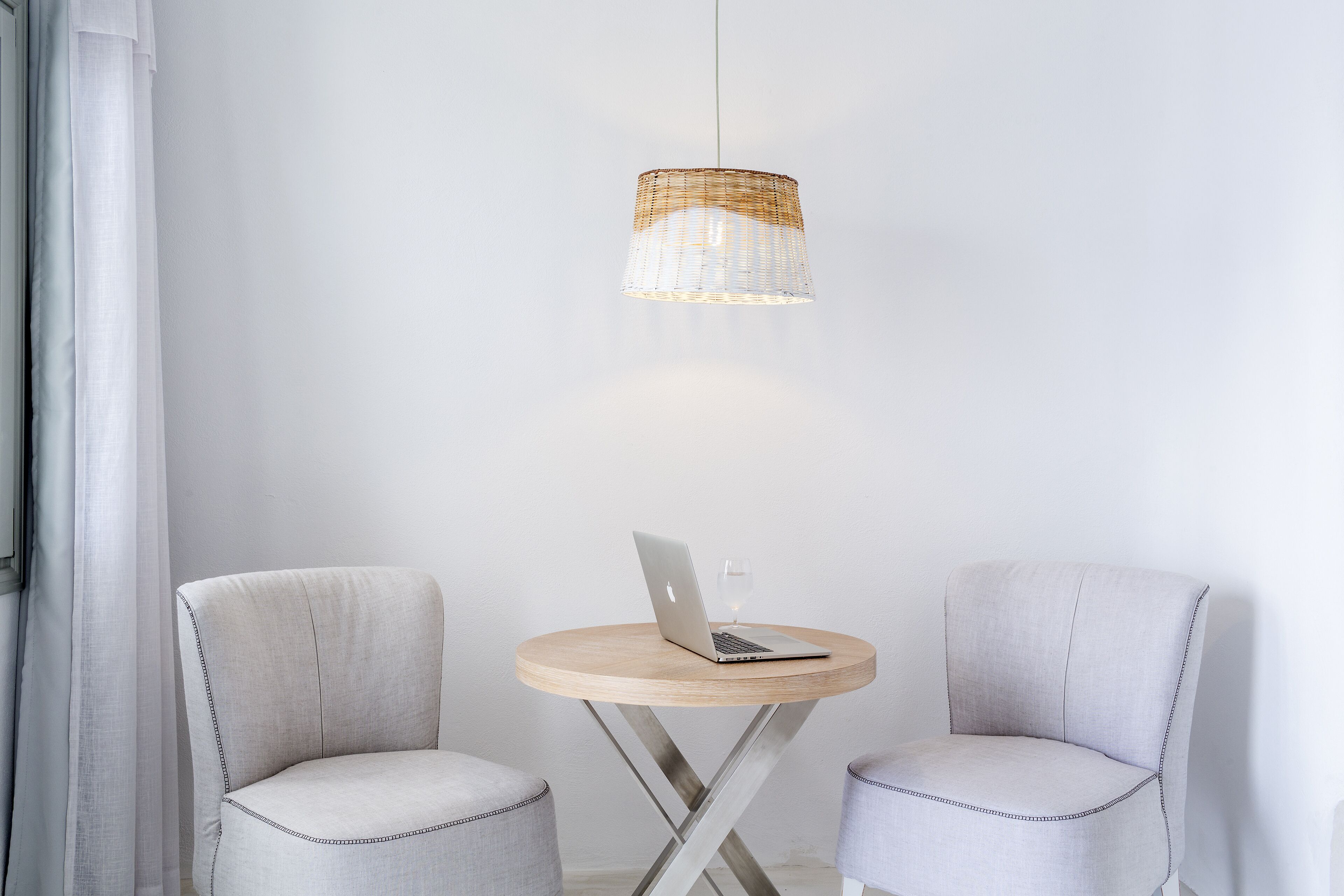 Una habitación con dos sillas, una mesa redonda con una computadora portátil y un vaso, y una lámpara colgante.