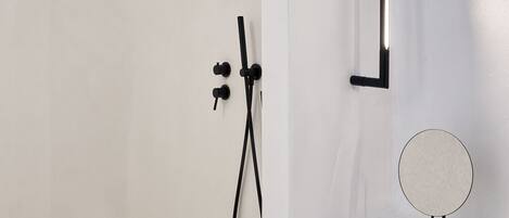 A minimalist bathroom with a freestanding shower, a handheld showerhead, a towel rack, and a round mirror on a countertop.