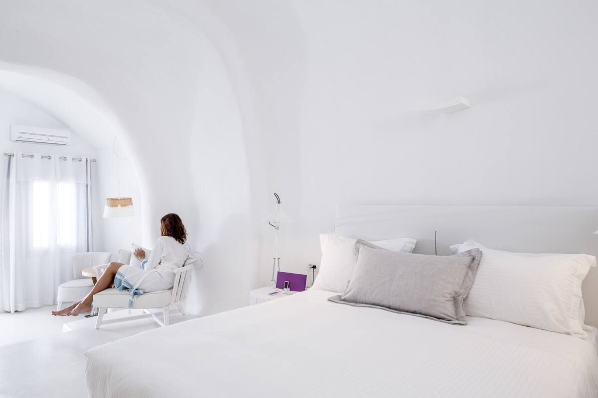 A modern hotel room with a large bed, a sitting area, and a window with curtains.