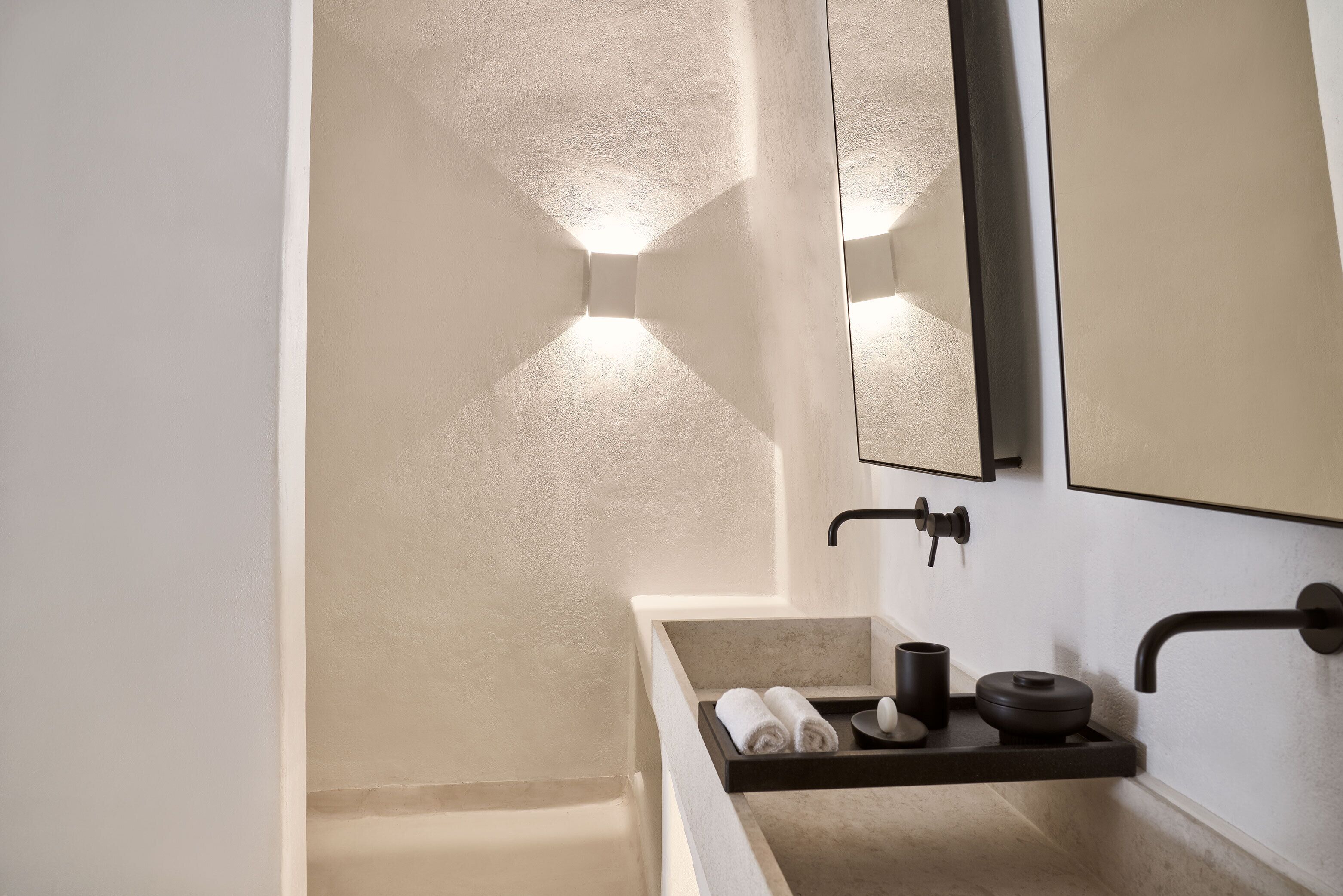 A modern bathroom with a beige wall, a rectangular sink with a black countertop, and a mirror above it.
