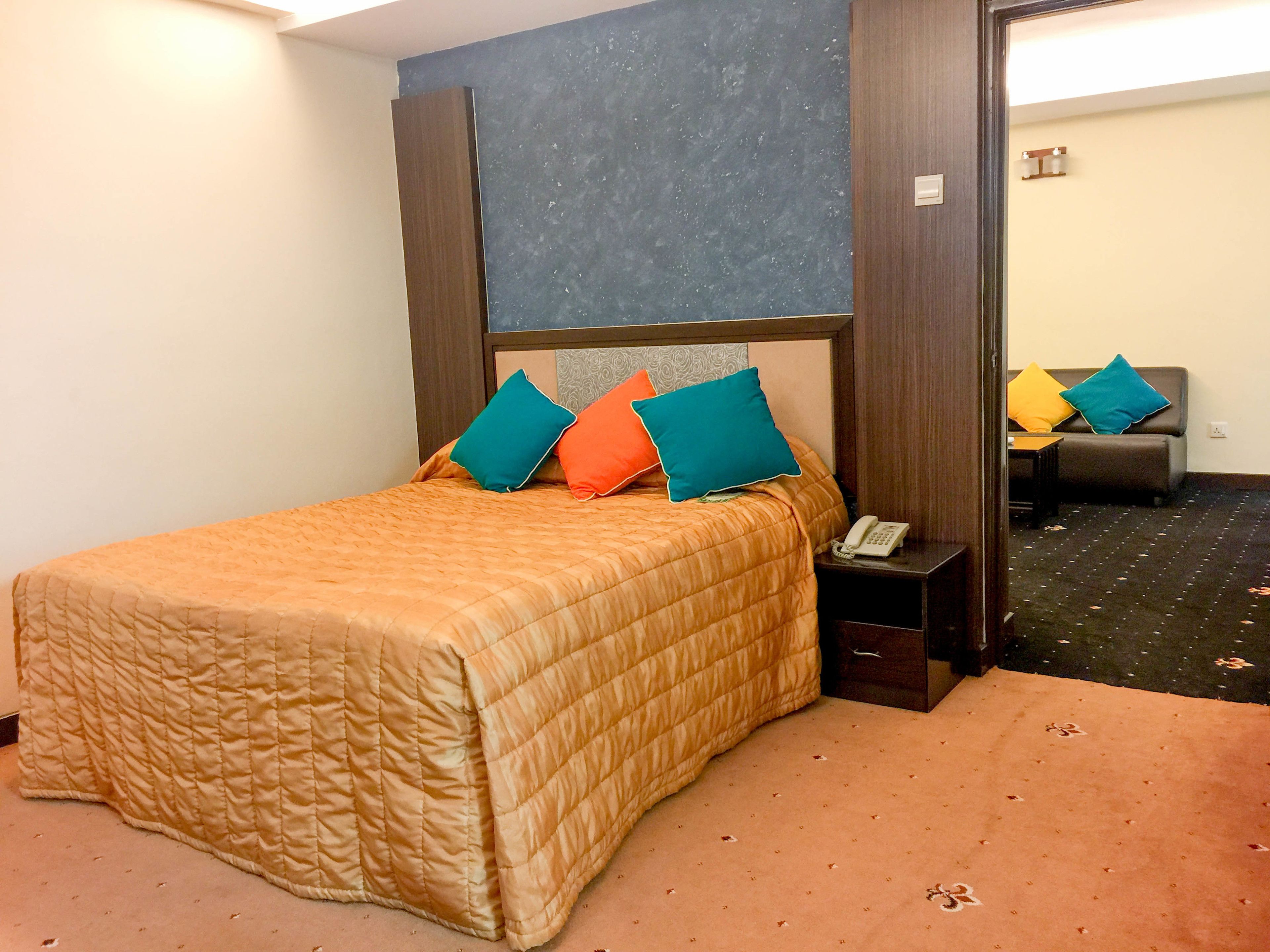 Habitación de hotel con cama, mesita de noche con teléfono y sofá al fondo.