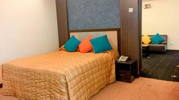 Habitación de hotel con cama, mesita de noche con teléfono y sofá al fondo.