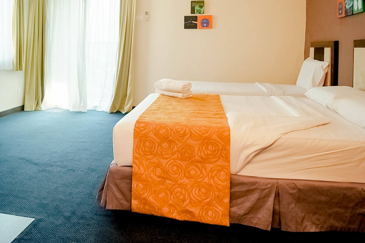 A hotel room with two beds, a blue carpet, beige walls, and a window with curtains.