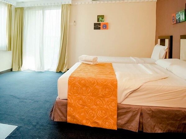 A hotel room with two beds, a blue carpet, beige walls, and a window with curtains. - Hotel Taiping Perdana (Taiping)
