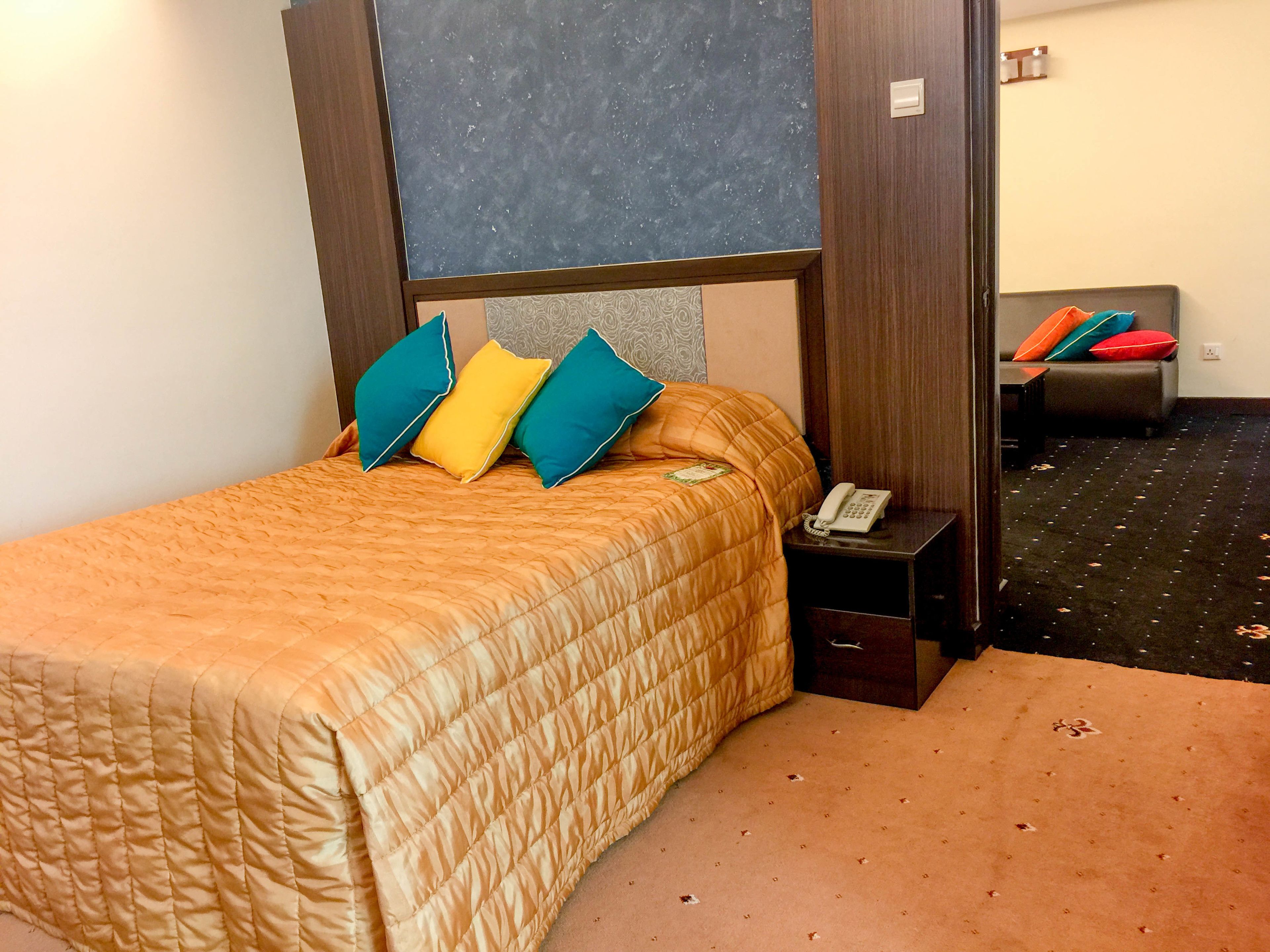 A hotel room with a bed, a bedside table with a phone, and a sofa in the background.