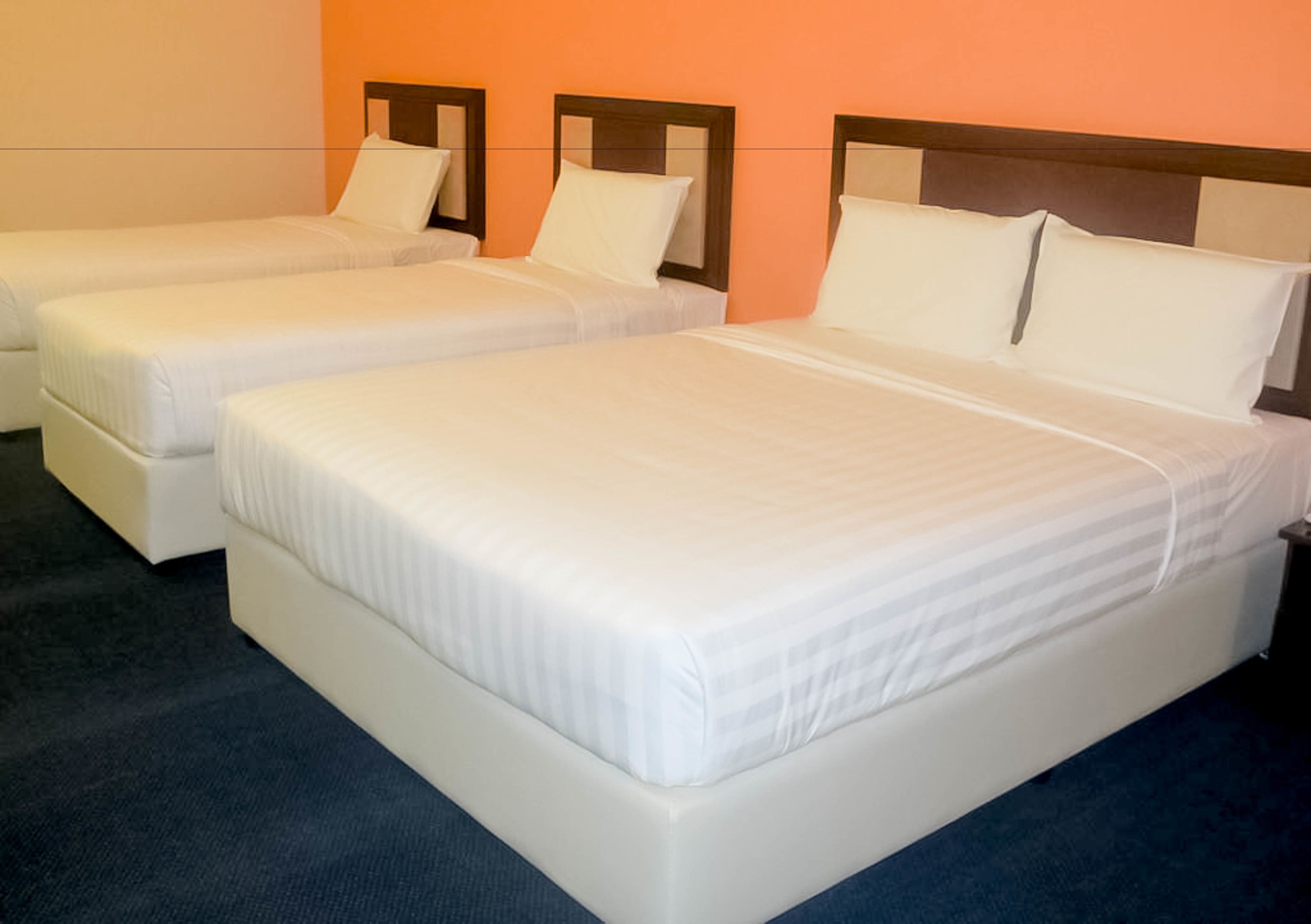 A hotel room with three single beds, each with a wooden headboard and white bedding.