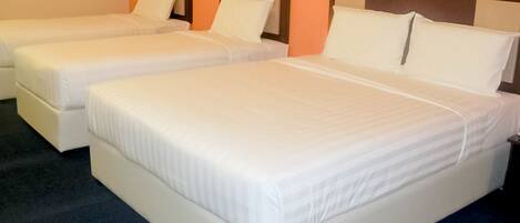 A hotel room with three single beds, each with a wooden headboard and white bedding.