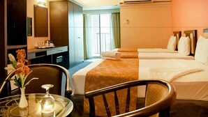 Habitación de hotel con escritorio, dos camas, una silla, una mesa con un jarrón y una ventana con cortinas.