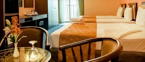 Ein Hotelzimmer mit Schreibtisch, zwei Betten, einem Sessel, einem Tisch mit Blumenvase und einem Fenster mit Vorhängen.