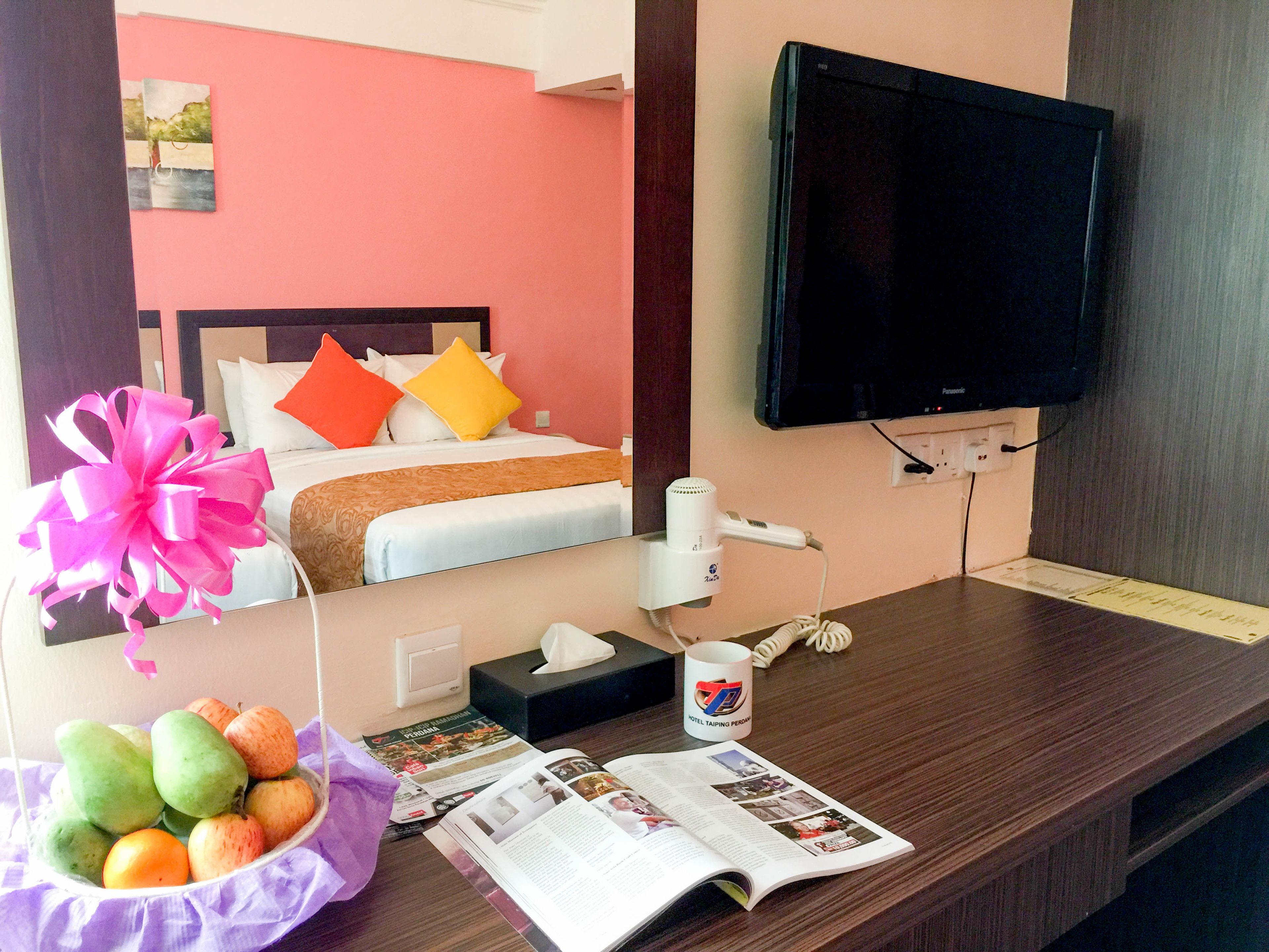 A hotel room with a bed, a TV, a desk with a magazine, a tissue box, and a hairdryer.