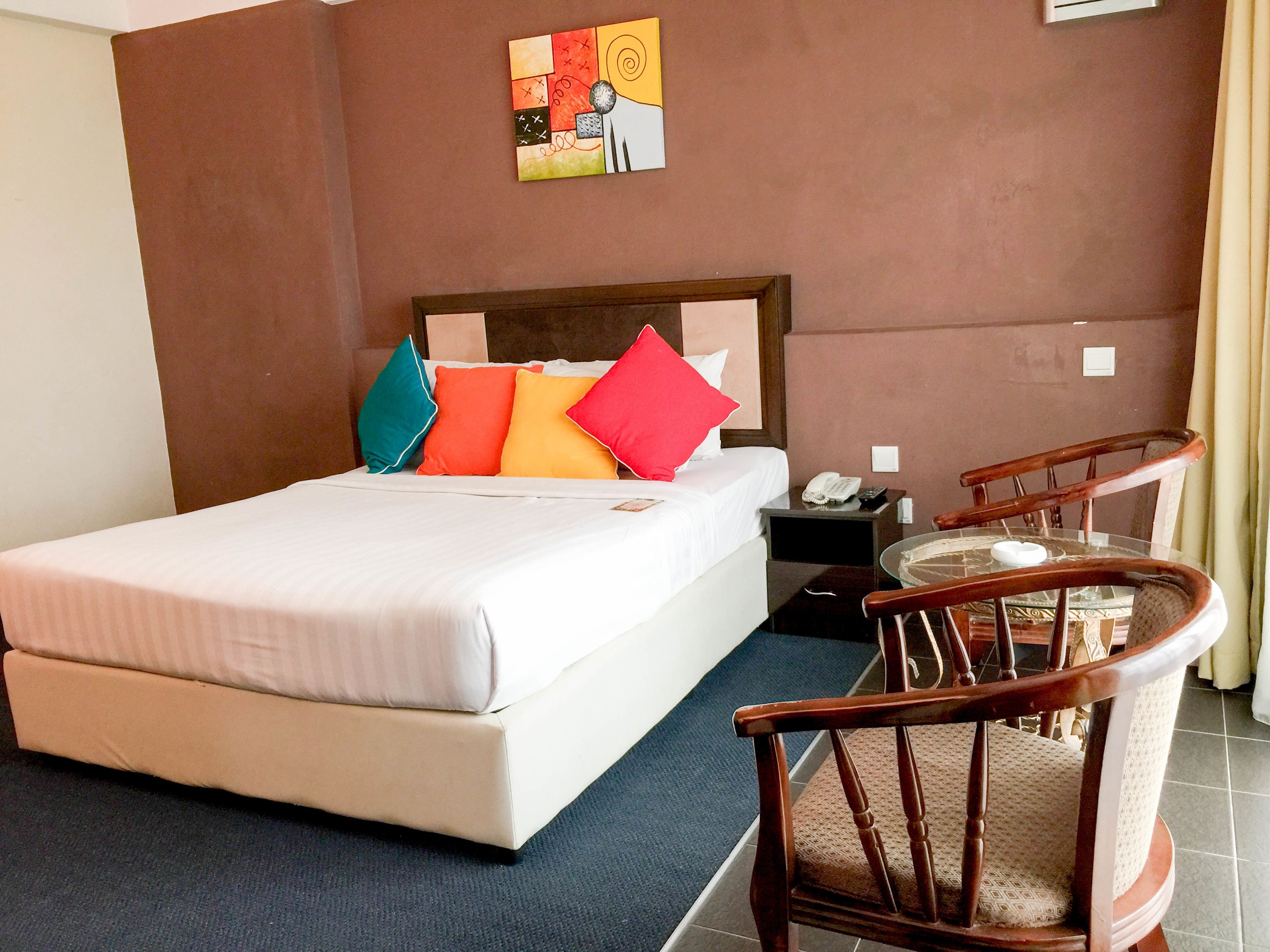 Une chambre d’hôtel avec un lit, une table de chevet avec un téléphone, une chaise et une petite table avec une tasse.