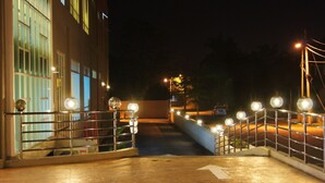 Vista nocturna de una escalera con barandillas y luces, que conduce a un edificio con grandes ventanales.