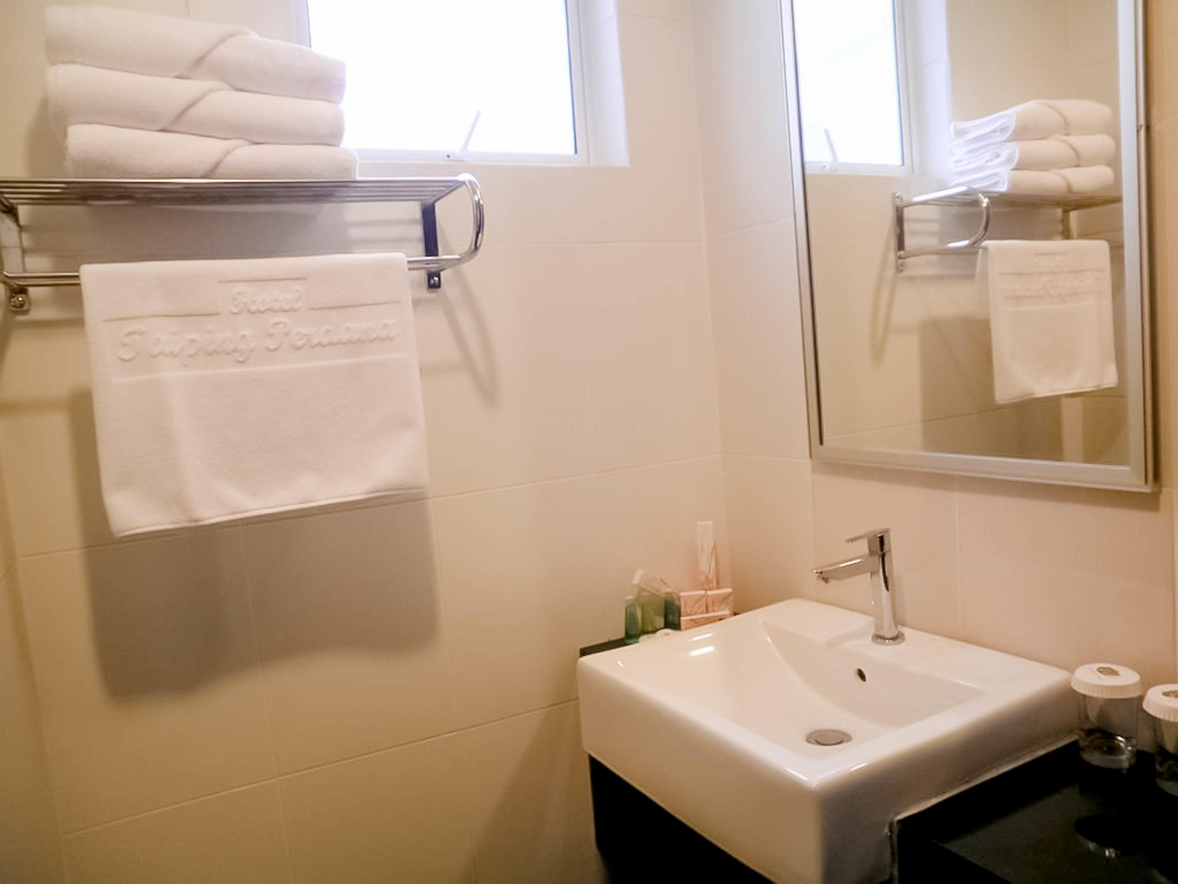 Un baño con un lavamanos blanco, un perchero con toallas dobladas y un espejo que refleja las toallas.
