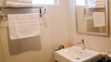 A bathroom with a white sink, a towel rack with folded towels, and a mirror reflecting the towels.