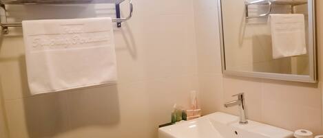 Un baño con un lavamanos blanco, un perchero con toallas dobladas y un espejo que refleja las toallas.