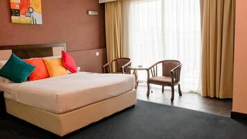 A hotel room with a bed, a chair, a small table, and a painting on the wall.
