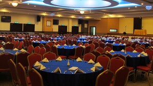 Un salón de conferencias con varias mesas redondas, sillas rojas y manteles azules.