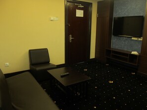Habitación de hotel con un sofá negro, una mesita, un control remoto, una puerta con un aviso y un televisor montado en una pared azul.
