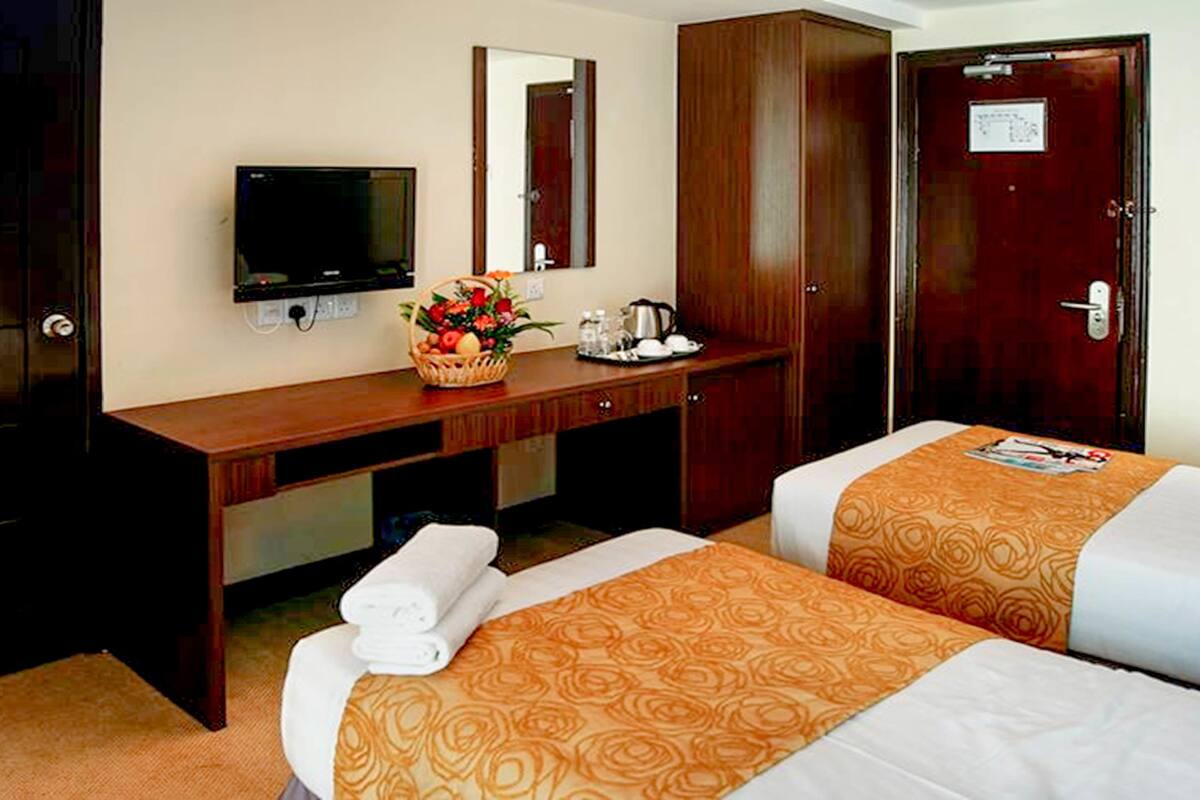 A hotel room with two beds, a desk with a television, a mirror, and a wooden wardrobe.