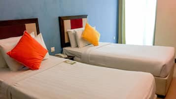 Two single beds with white bedding and pillows, a bedside table with a phone, and a blue wall with a light switch.