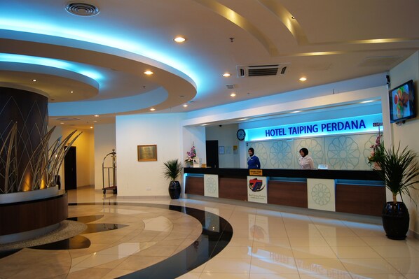 Zona de recepción de hotel con diseño moderno, que incluye un mostrador de recepción, un reloj digital y un letrero para Hotel Taiping Perdana.
