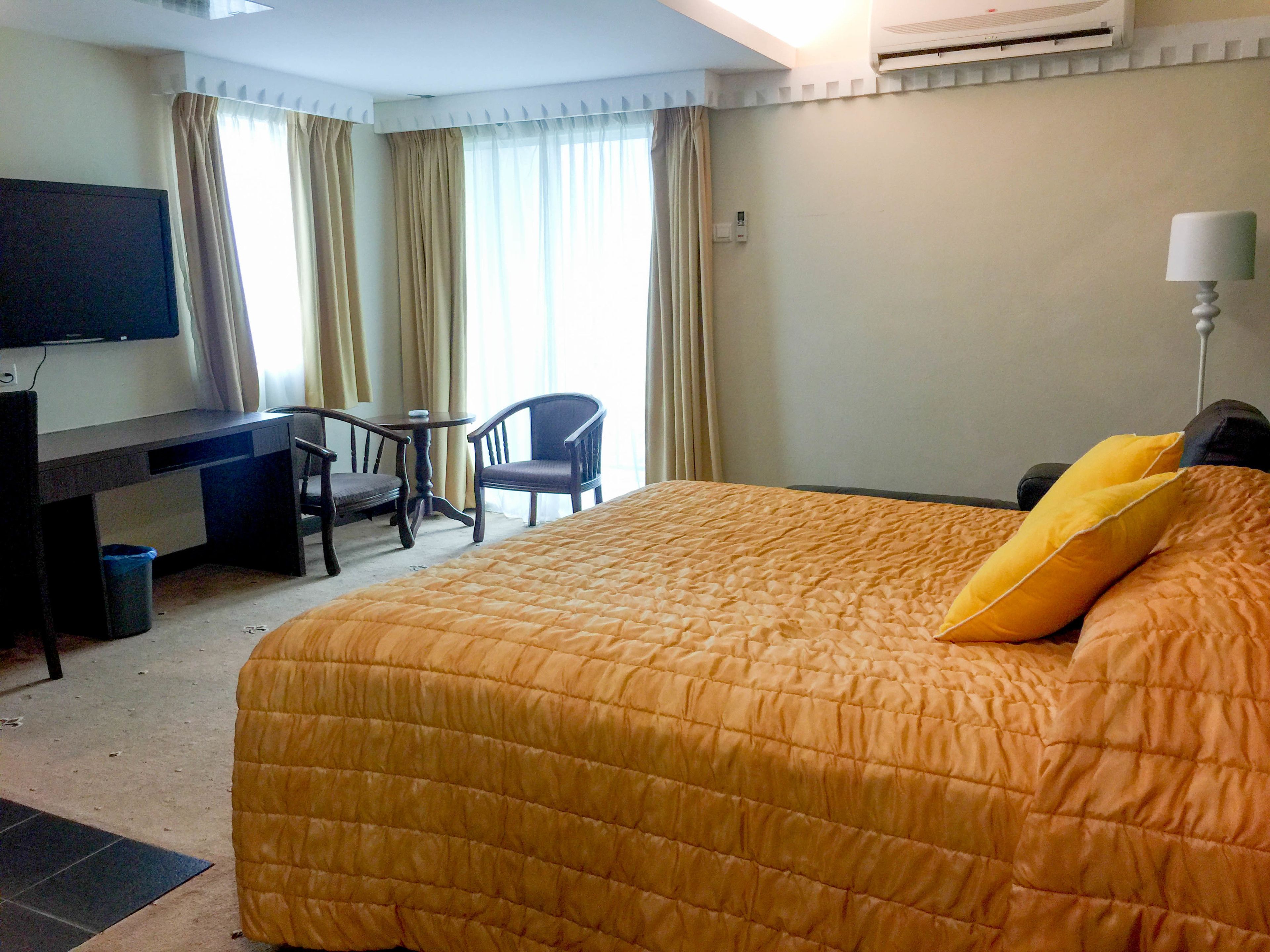 Una habitación de hotel con cama, escritorio, silla, televisor y cortinas.
