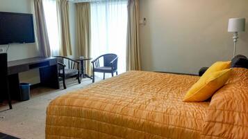 Una habitación de hotel con cama, escritorio, silla, televisor y cortinas.