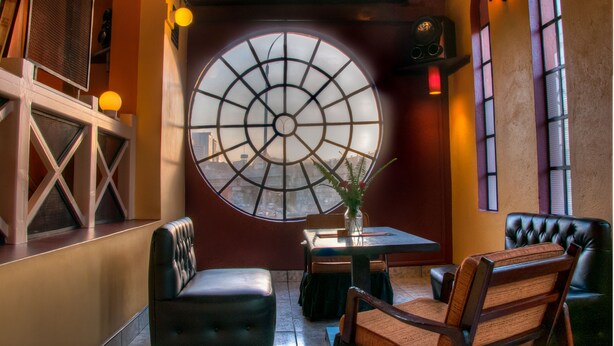 A restaurant with a large circular window, cushioned seating, and a small table with a vase. - Kahama Hotel (Nairobi)