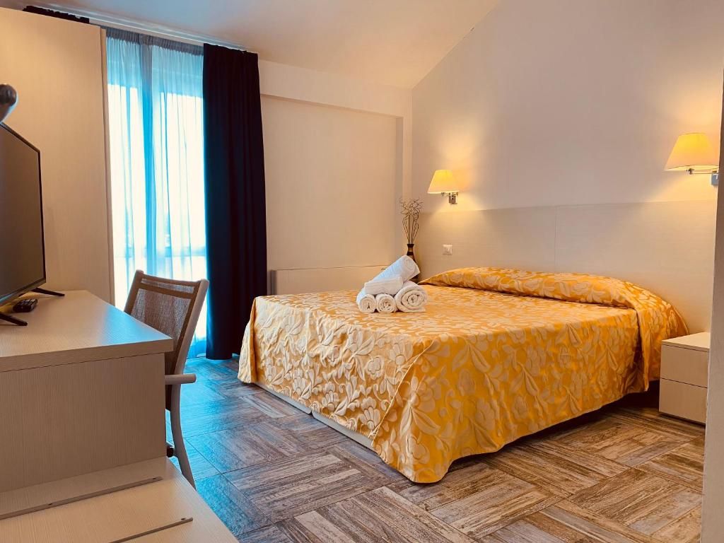 Una camera d'albergo con un letto, una scrivania, una sedia, una lampada e una finestra con tende.