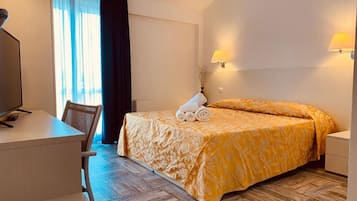 Una camera d'albergo con un letto, una scrivania, una sedia, una lampada e una finestra con tende.