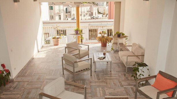 A spacious balcony with a modern outdoor seating area, including a sofa, chairs, and a coffee table. There are potted plants and a view of neighboring buildings. - Hotel Mûita di Mari (Santa Teresa di Gallura)